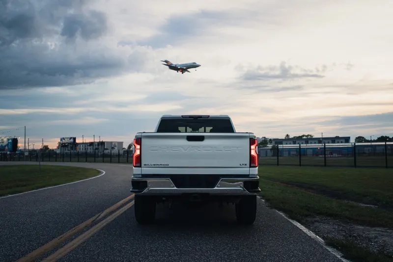Rear of a white Chevy Silverado 3500HD with a jet flying overhead