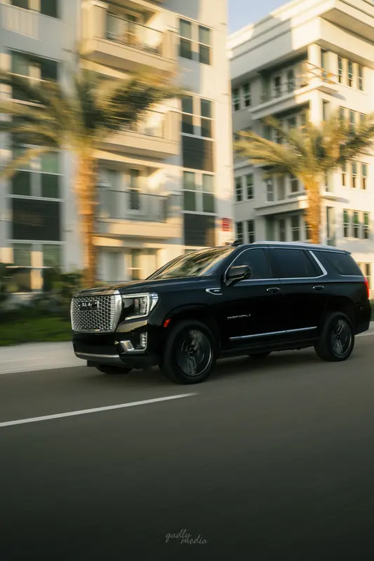 Detailed black GMC Yukon Denali rolling past palm trees